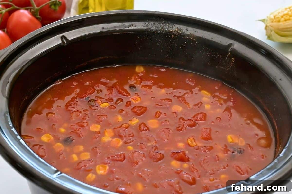 Slow cooker with cooked tortilla soup made with chicken breasts, beans, and corn, and a spiced tomato broth.
