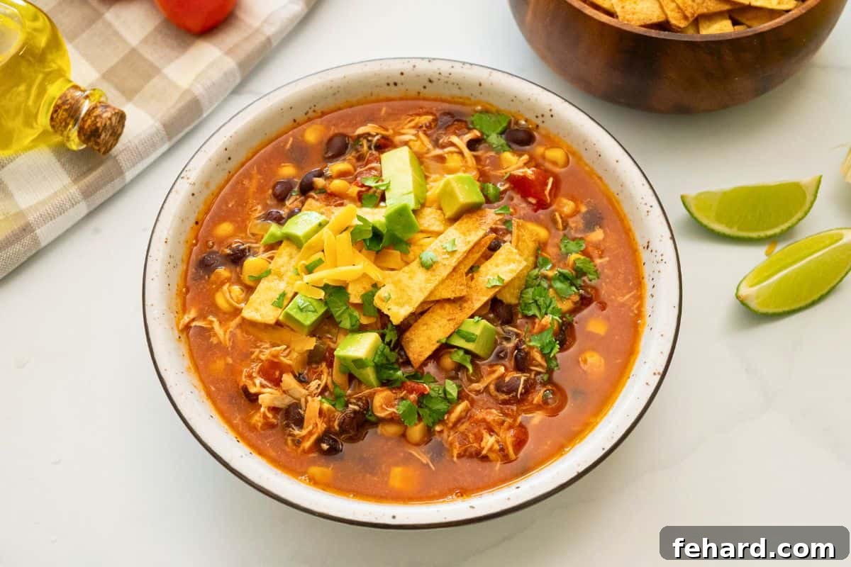 Bowl of Chicken Tortilla Soup topped with diced avocado, homemade tortilla strips, shredded cheese and minced cilantro.