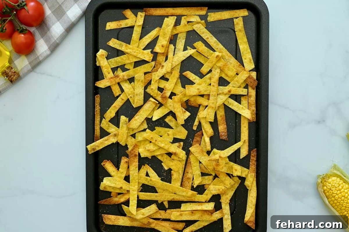 Baked crispy corn tortilla stirps on baking sheet after being coated in oil, seasonings, and baked until crispy.