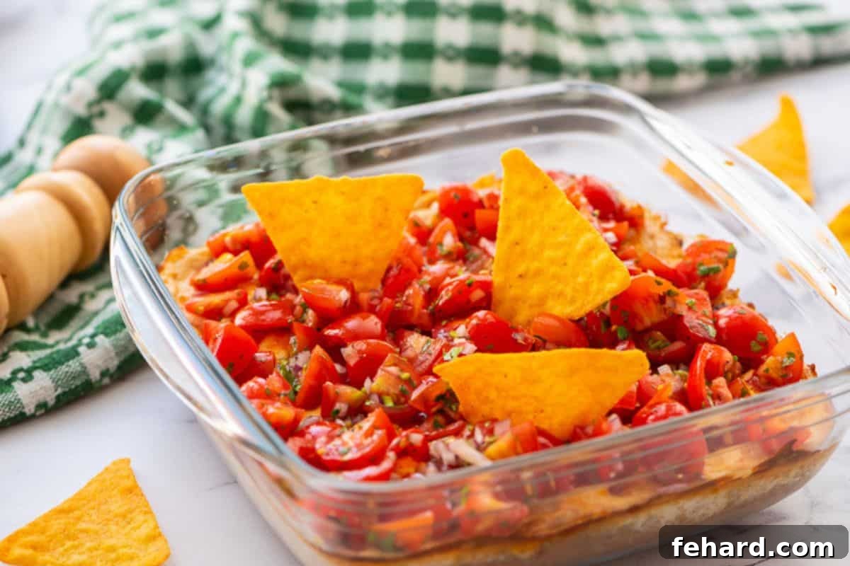 Creamy layered taco dip baked in glass dish topped with fresh pico and tortilla chips.