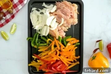 Sliced chicken breasts, bell peppers, sliced onions on rimmed sheet pan.