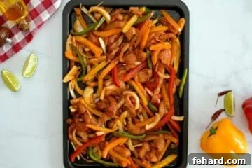Sliced chicken breast, raw bell peppers, and yellow onion on sheet pan tossed with fajita seasoning.