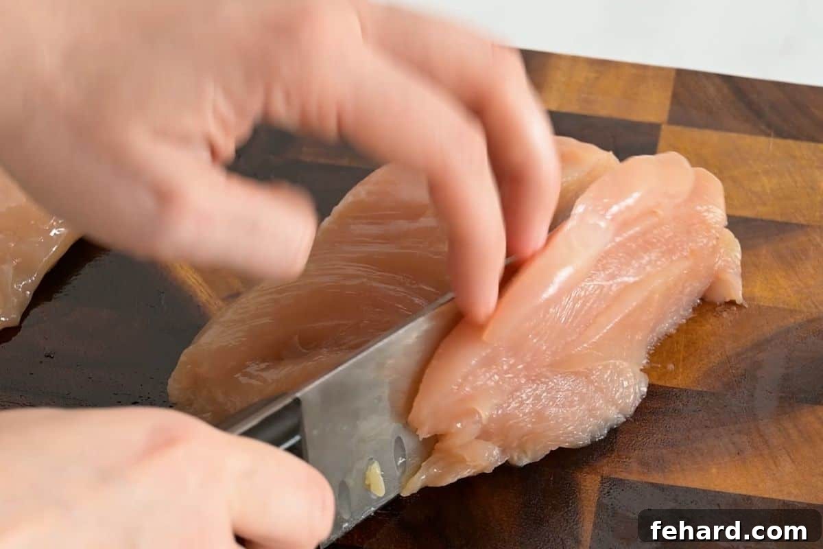 Chef precisely slicing boneless, skinless chicken breasts into half-inch strips against the grain, preparing for sheet pan chicken fajitas.