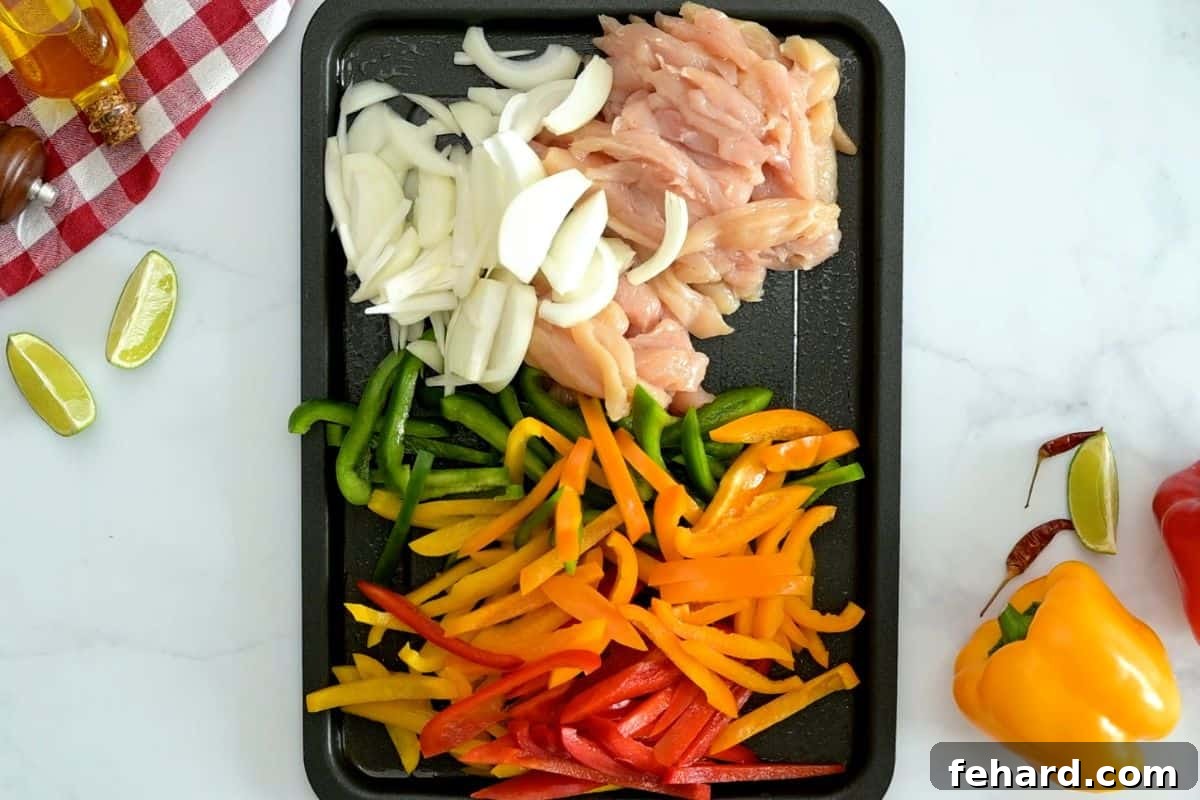 Raw sliced chicken breasts, colorful bell peppers, and yellow onions arranged on a large rimmed sheet pan, ready for seasoning.