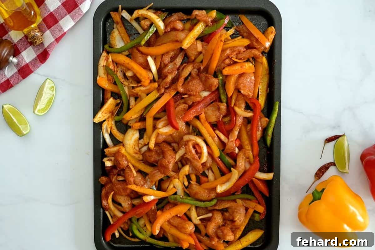 Close-up of sliced chicken breast, raw bell peppers, and yellow onion on a sheet pan, perfectly tossed and coated with vibrant fajita seasoning.