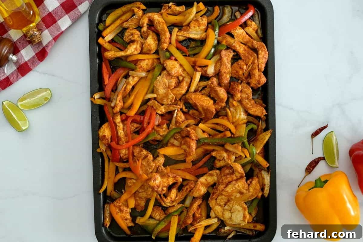 Baked sheet pan chicken fajitas, featuring perfectly roasted chicken breasts, softened bell peppers, and caramelized onions, fresh out of the oven.