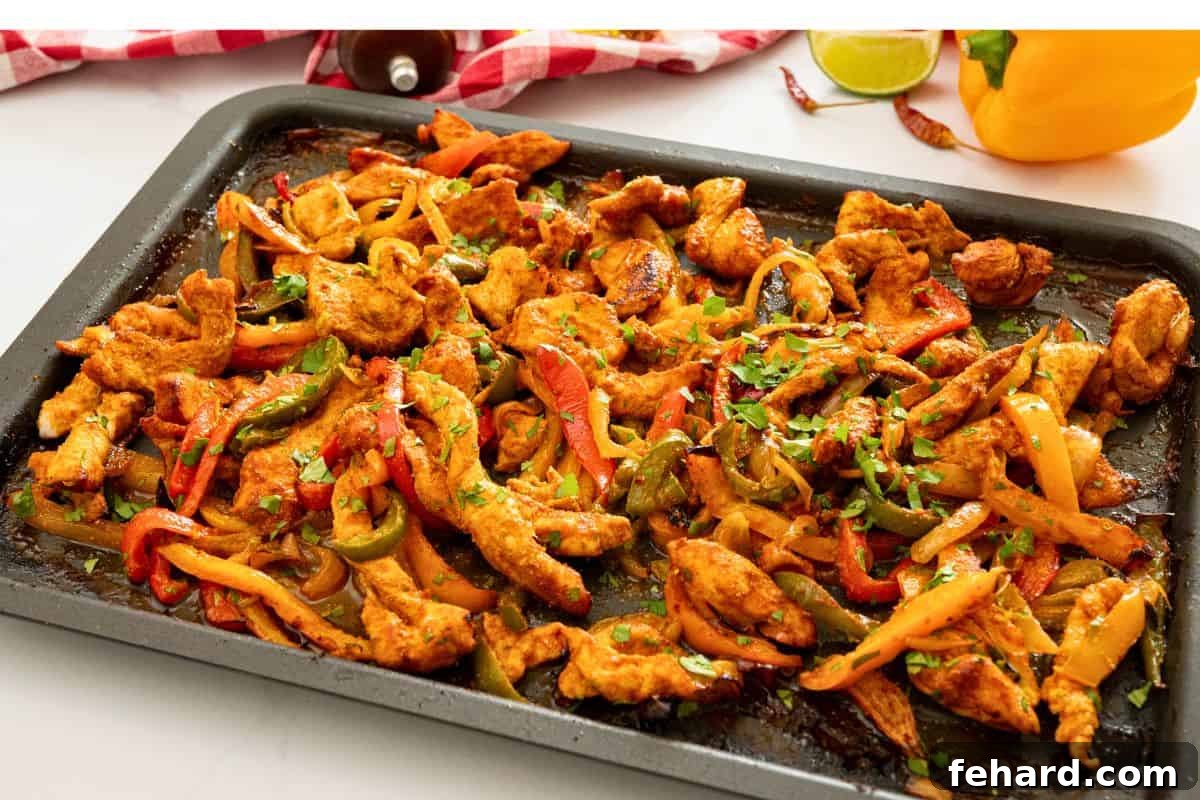 Hot sheet pan chicken fajitas, roasted with peppers and onions, being finished with a generous sprinkle of lime zest and fresh cilantro, enhancing flavor.