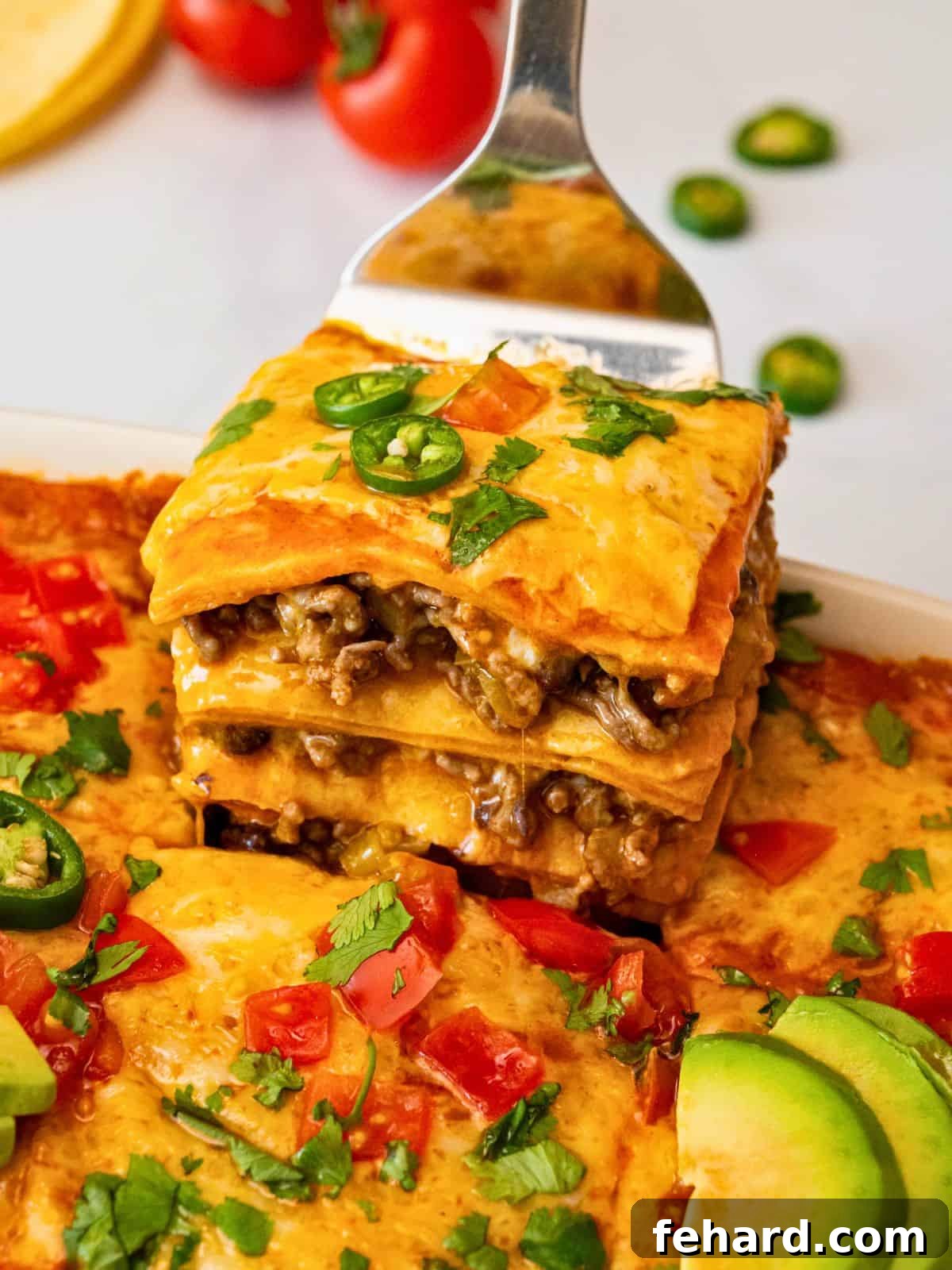 A spatula lifting a perfect slice of layered beef enchilada casserole from a baking dish, revealing the delicious layers of ground beef, cheese, tortillas, and red sauce.