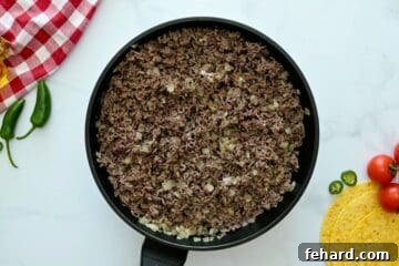 Lean ground beef being browned in a skillet with minced onion and garlic to create the base for the enchilada filling.