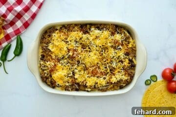 A close-up view of the layering process for the beef enchilada casserole, showing beef, sauce, and cheese over tortillas.
