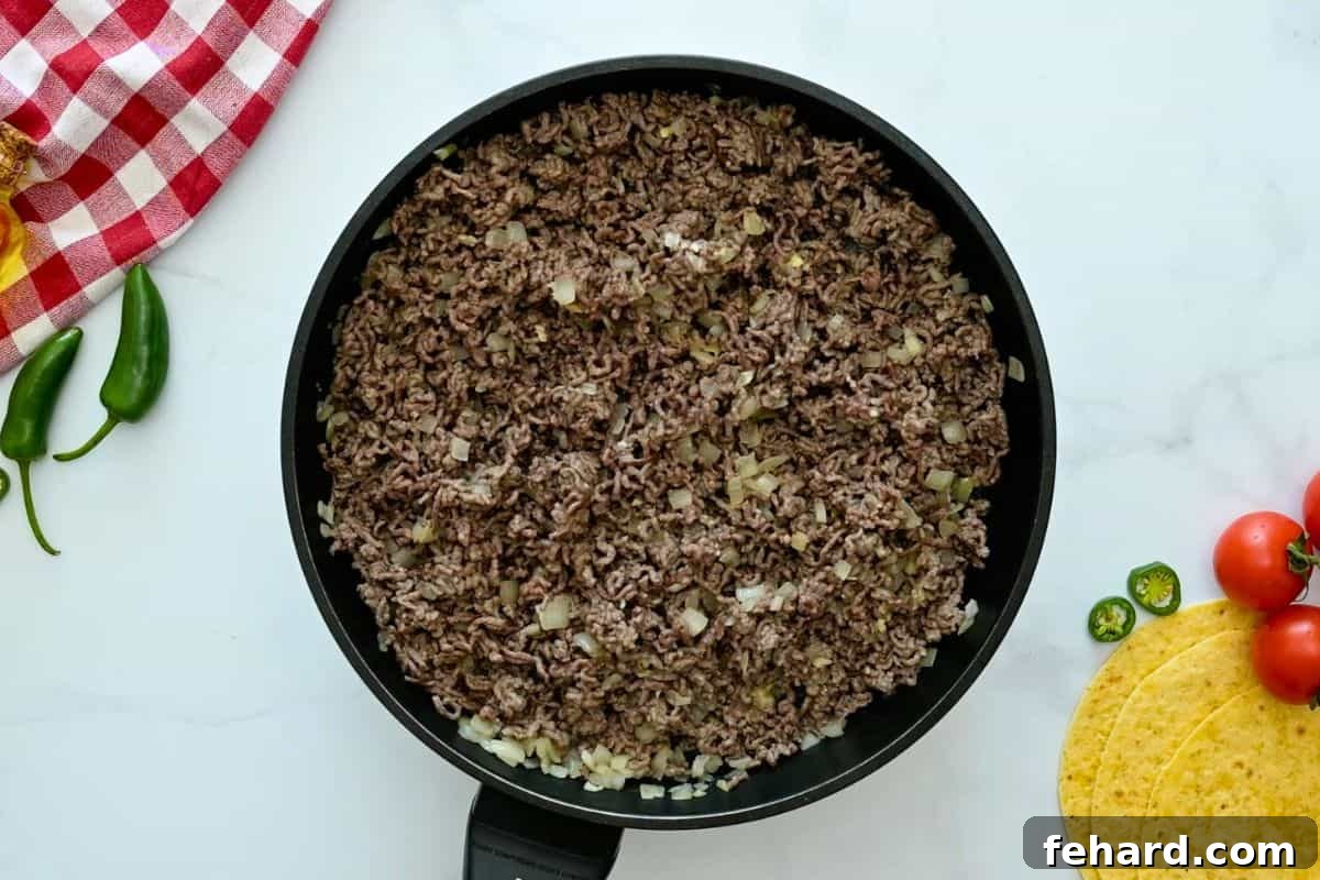 Ground beef and onions being browned in a skillet, creating the flavorful base for the enchilada casserole filling.