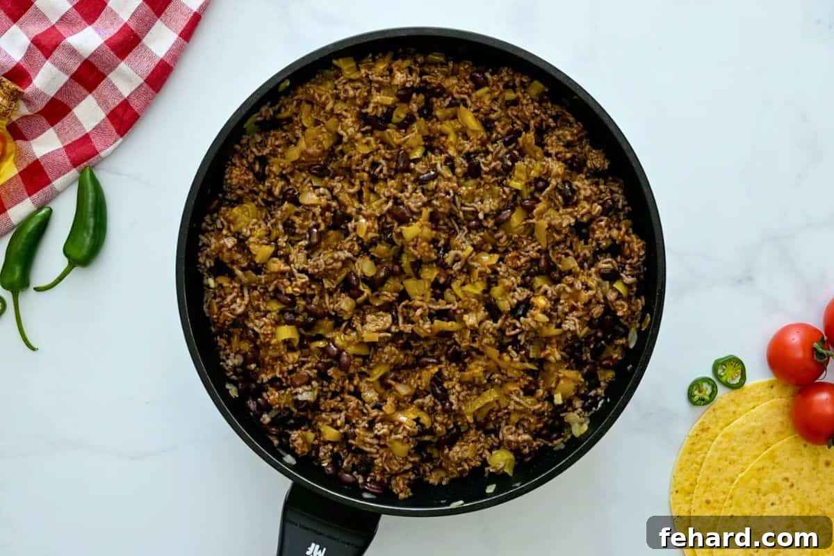 The fully prepared enchilada filling in the skillet, with ground beef, beans, green chiles, and sauce mixed together.