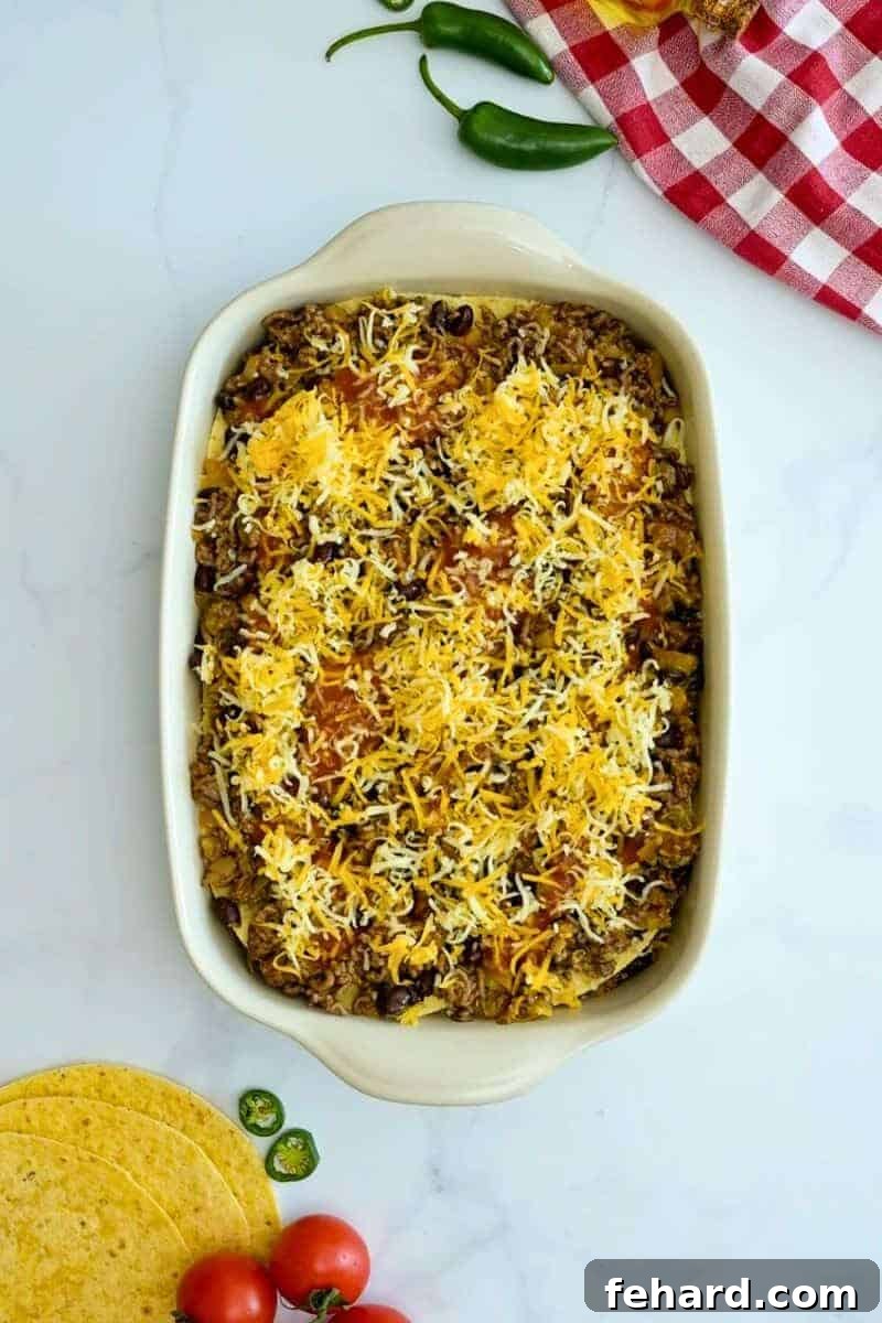 The casserole dish with layers of beef filling, sauce, and cheese being added on top of the tortillas.