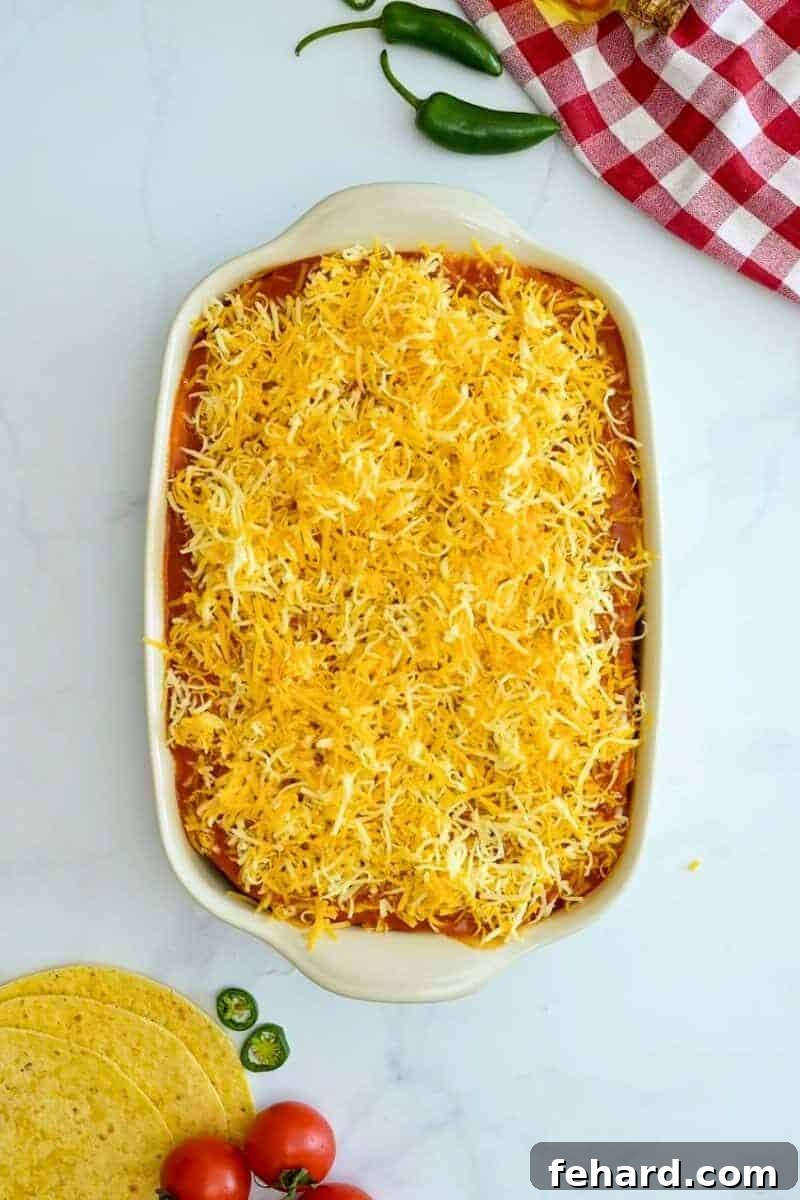 The fully assembled beef enchilada casserole, topped with the final layer of sauce and cheese, ready for the oven.
