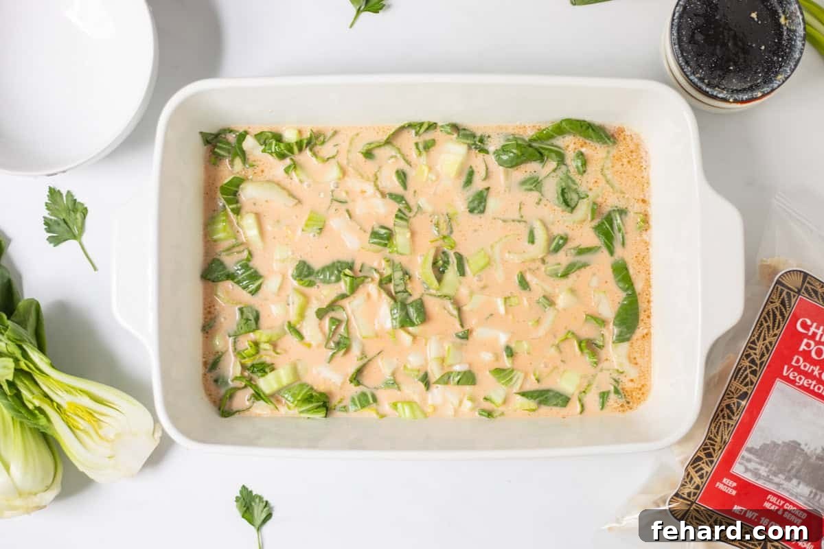 Sliced bok choy mixed into coconut milk, soy sauce, sesame oil, curry paste, and rice vinegar in 9x13 inch baking dish next to bag of frozen chicken and pork potstickers.