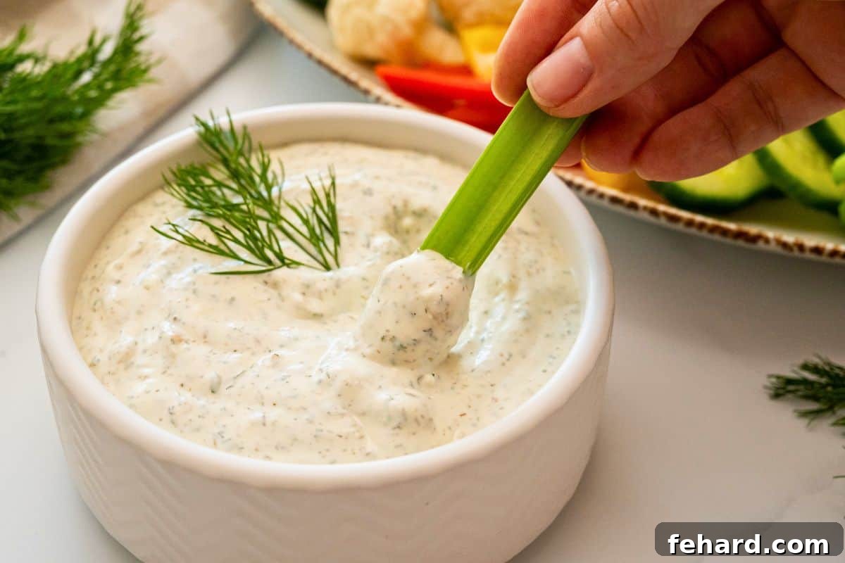 Stalk of celery being dipped into homemade dill dip made with sour cream and mayonnaise.