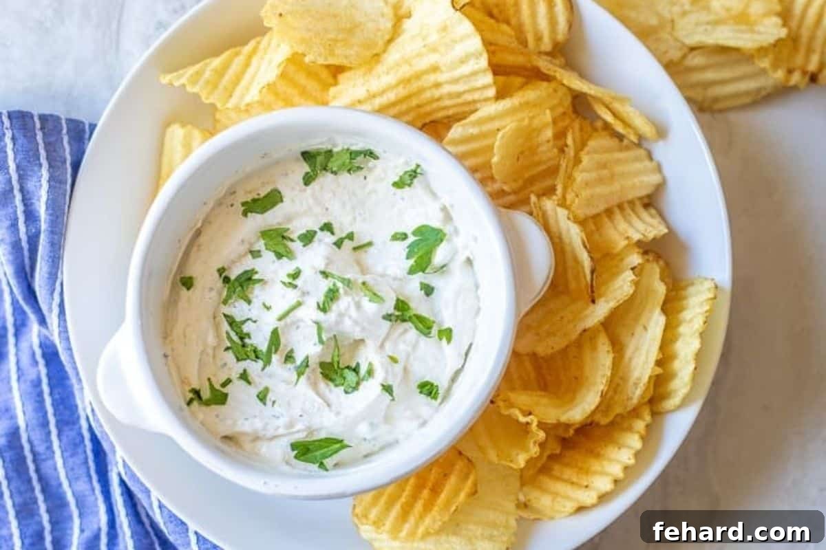 Bowl of chip dip made with dried seasonings and sour cream in bowl topped with fresh parsley served next to potato chips.