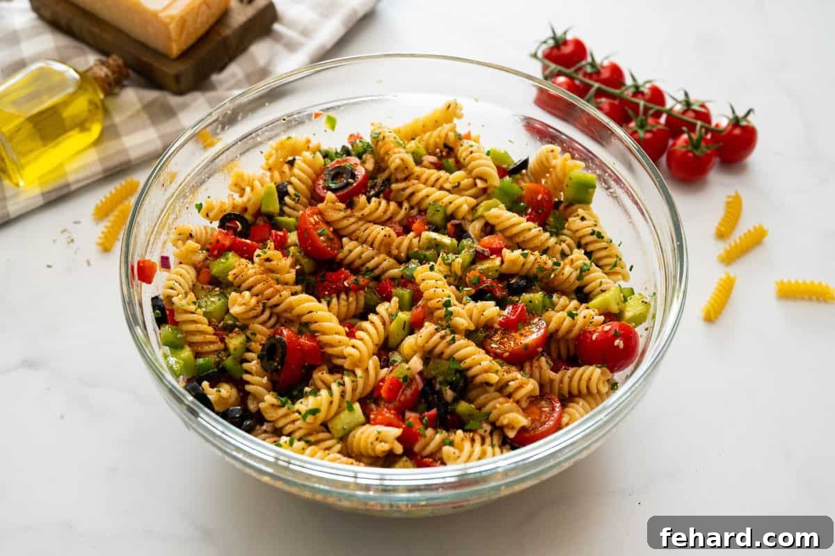 Mixing bowl with rotini noodles tossed with Italian dressing, peppers, cucumbers, olives, tomatoes, and salad supreme seasoning.