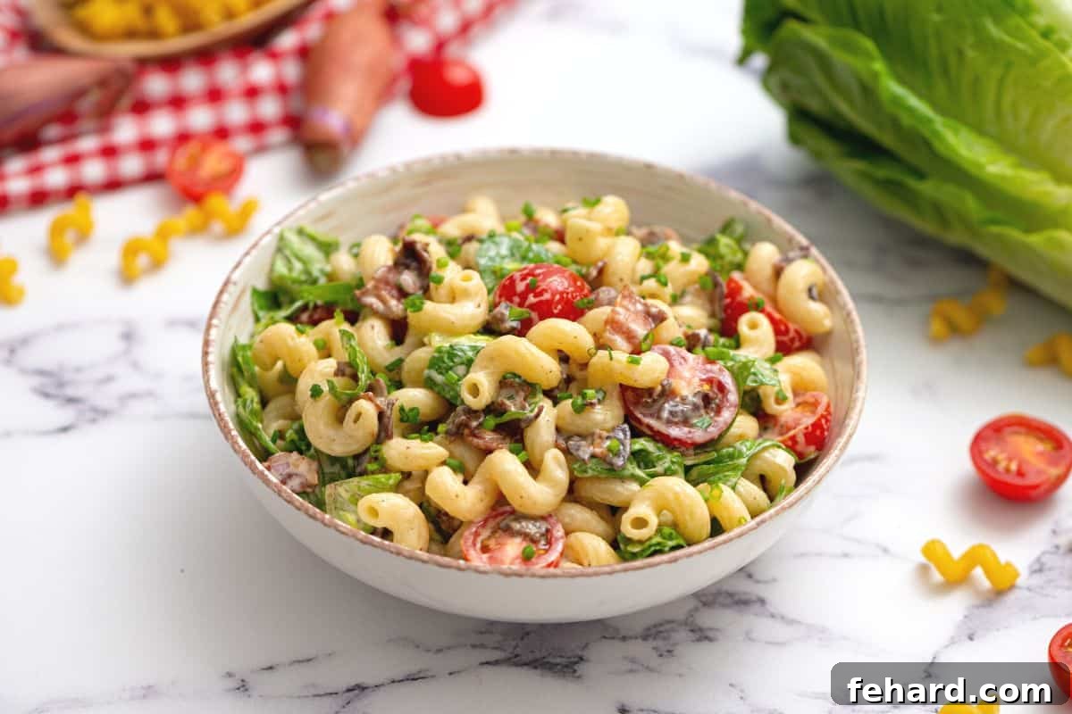 Bowl of creamy BLT Pasta Salad with grape tomatoes in background.
