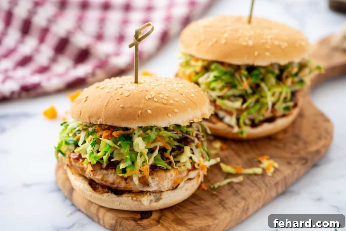 Two grilled BBQ chicken burgers made with BBQ sauce and cheese on platter topped homemade coleslaw served on sesame buns.