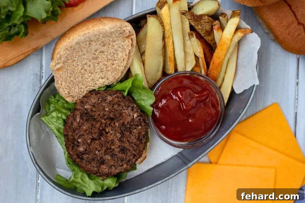 Homemade Black Bean Patty on Whole Wheat Bun next to lettuce, sliced cheese, and side of homemade fries.