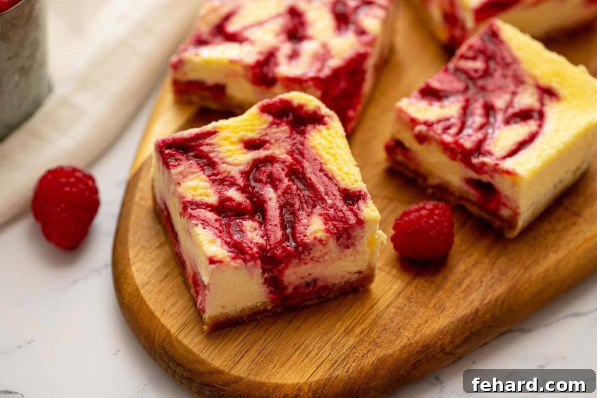 Sliced cheesecake bars on wooden cutting board revealing the raspberry swirl throughout the cheesecake batter.