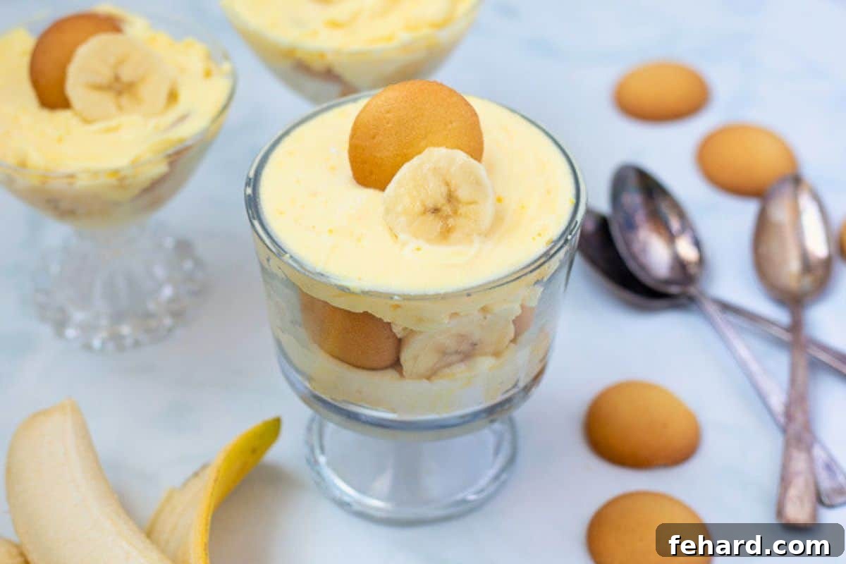 Homemade vanilla pudding layered with sliced bananas and vanilla wafters in mini trifle dishes next to fresh bananas and vanilla wafers.
