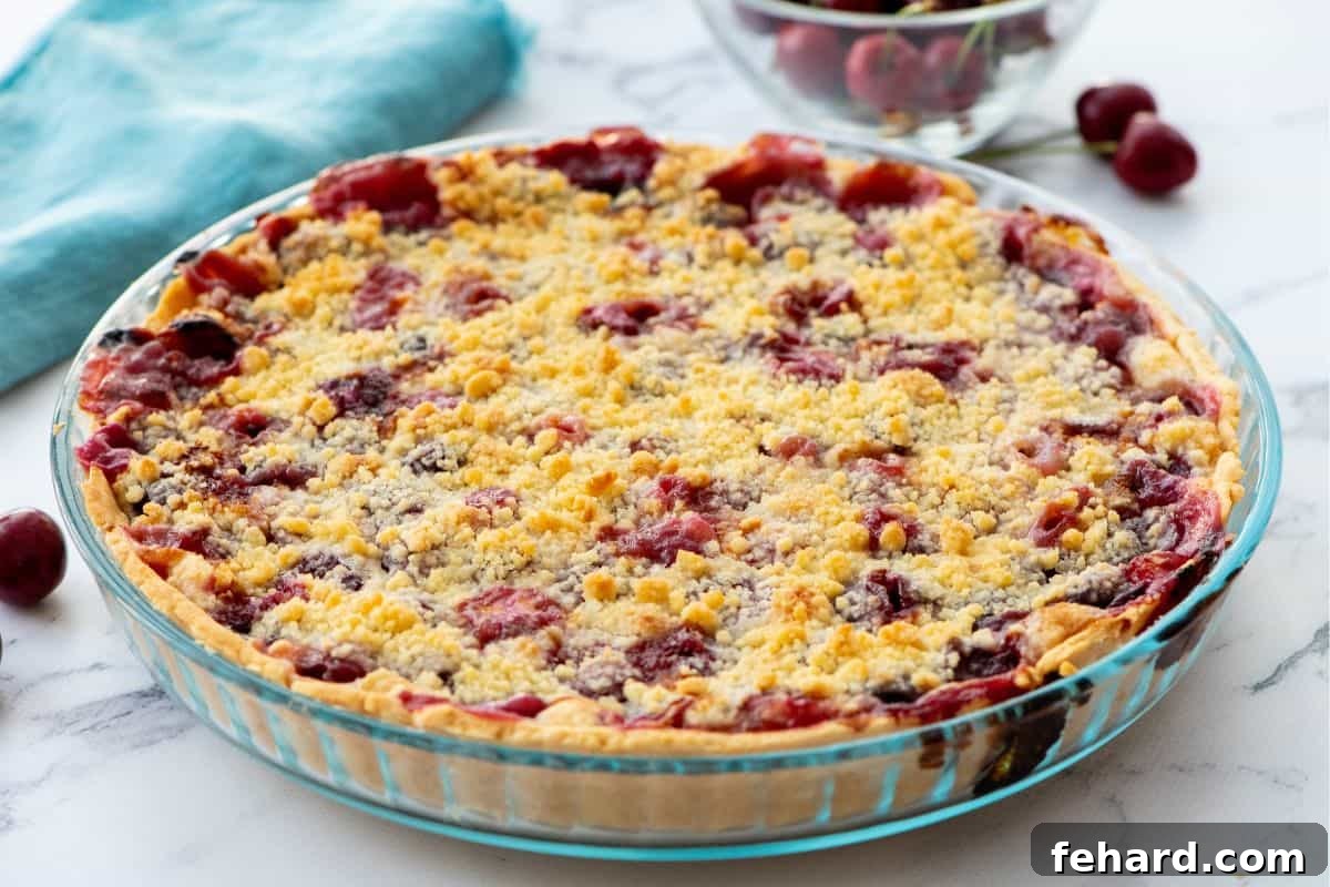Baked Cherry Crumble pie in clear baking dish next to fresh cherries.