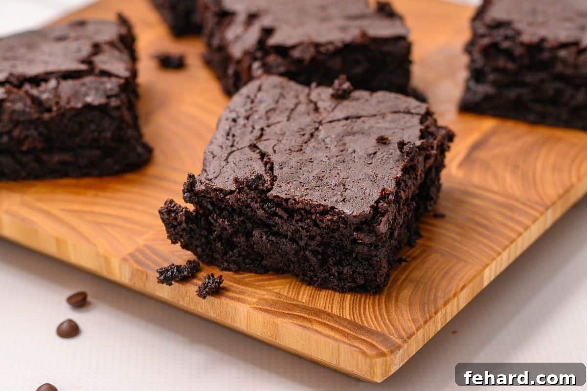 Sliced fudgy brownies on wooden cutting board with chocolate chips scattered around.