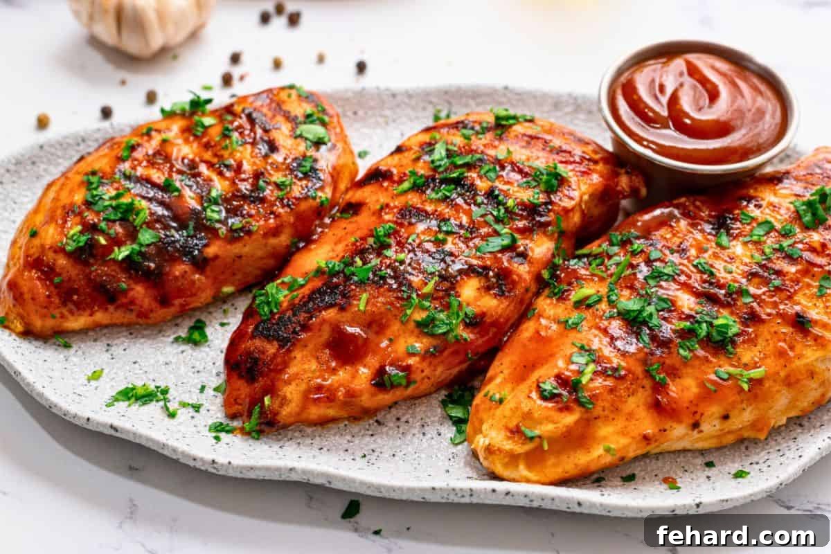 Three grilled BBQ chicken breasts on platter topped with parsley.