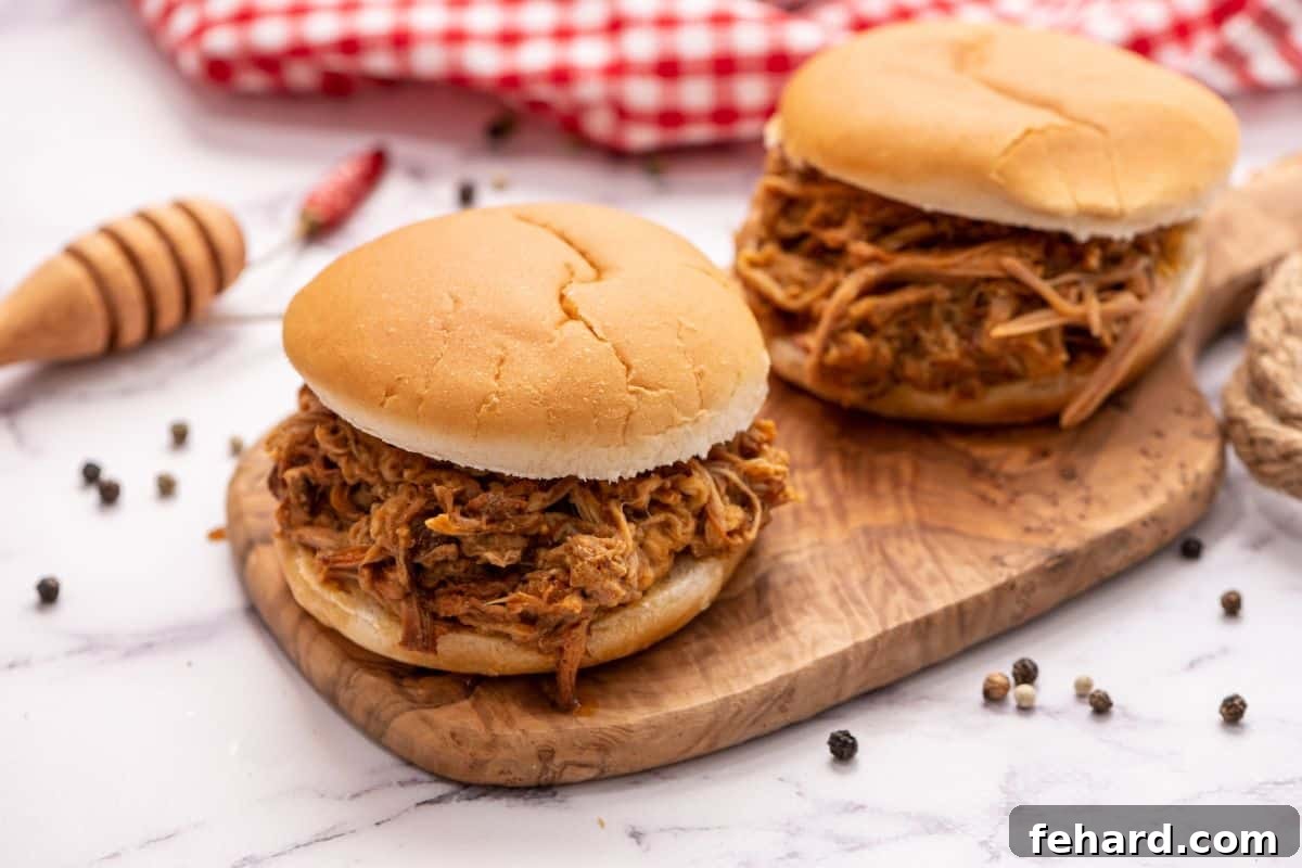 Slow Cooker shredded bbq pulled pork piled on two buns on wooden cutting board.