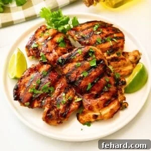Grilled cilantro lime chicken thighs on platter topped with fresh cilantro next to fresh lime wedges.