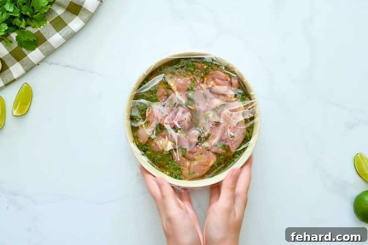 Chicken thighs in cilantro lime marinade covered with plastic wrap.
