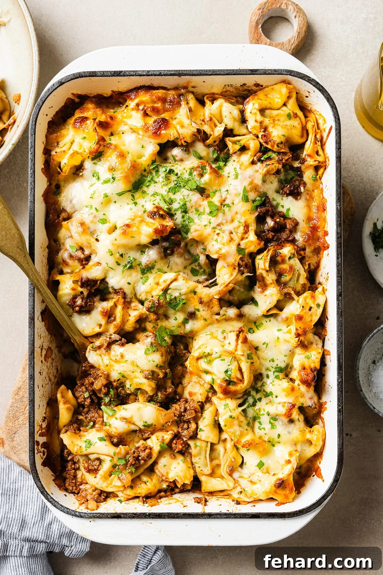 Cheesy Baked Tortellini with Savory Ground Beef Casserole 2 baked tortellini with ground beef in a white 9x13 baking dish, golden melted mozzarella on top, garnished with fresh parsley