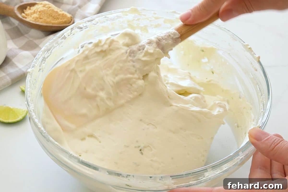 key lime pie recipe no eggs Fresh whipped cream being slowly folded into key lime cream cheese mixture using a spatula to lift up and over.