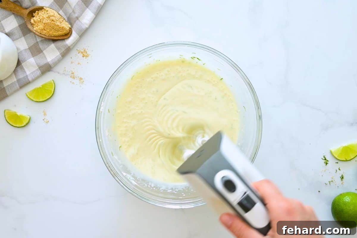 Recipe Key Lime Pie Handheld mixer mixing lime zest and sweetened condensed milk into cream cheese.