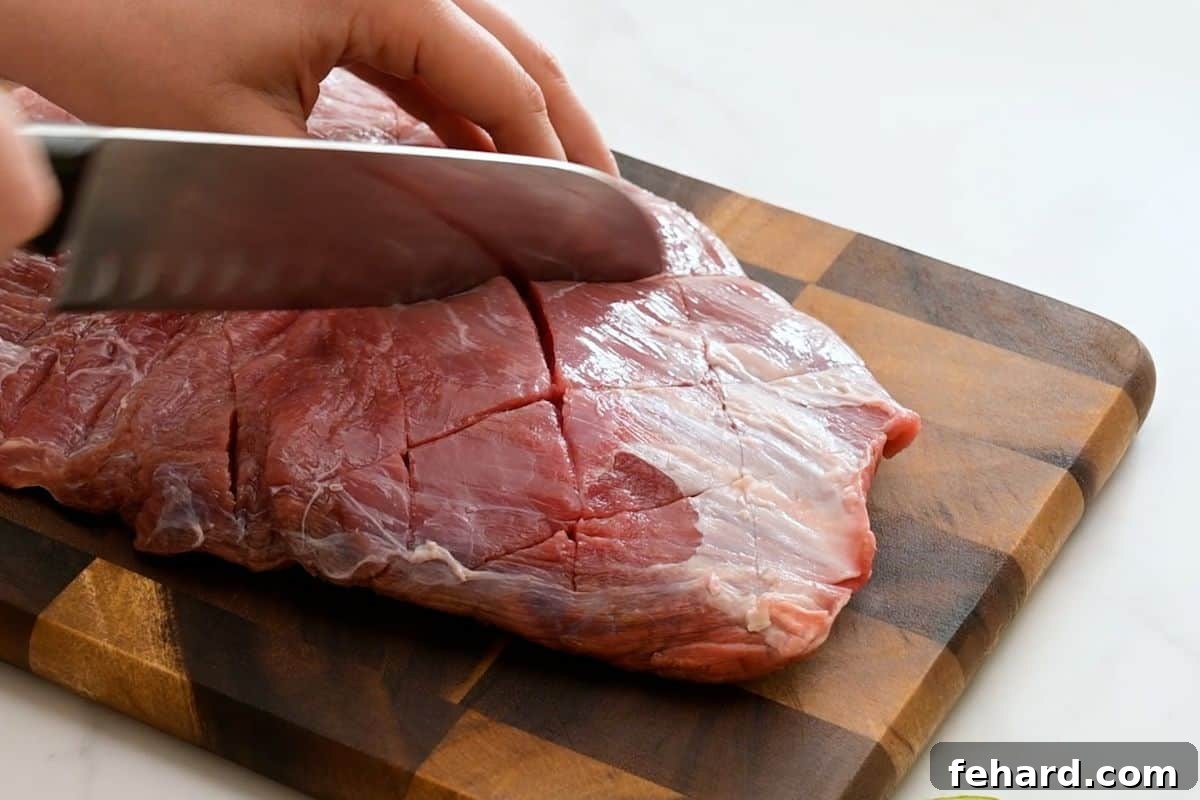 Chef's knife scoring flank steak with diagonal cuts before marinating.