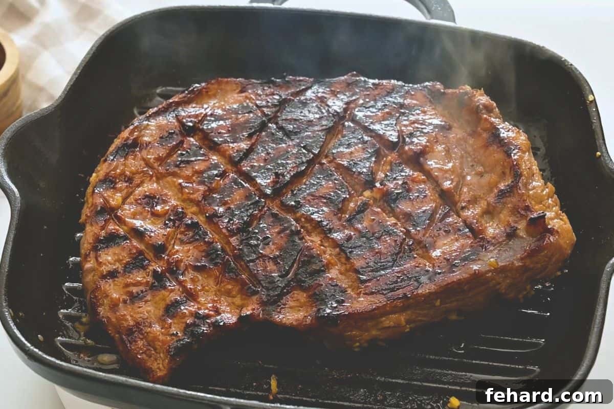 Marinated flank steak on grill plate partially grilled.
