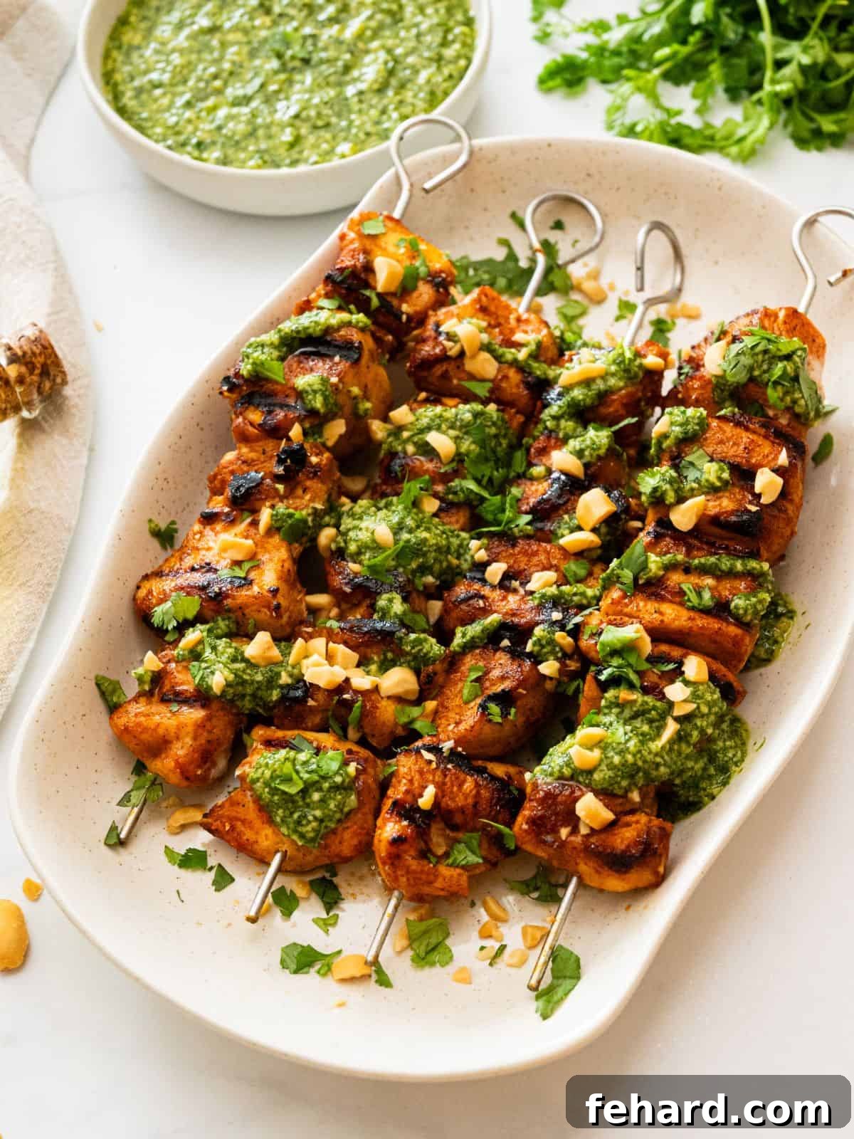 Grilled Chicken Kabobs Grilled chicken kabobs on white platter topped with cilantro pesto, fresh cilantro, and chopped peanuts.