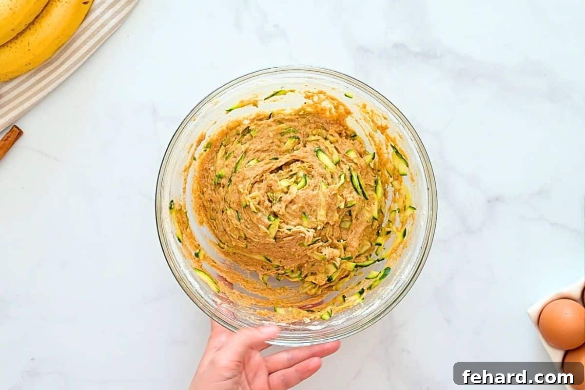 Zucchini Banana Loaf Shredded, squeezed zucchini folded into whole wheat flour quick bread batter in large mixing bowl.