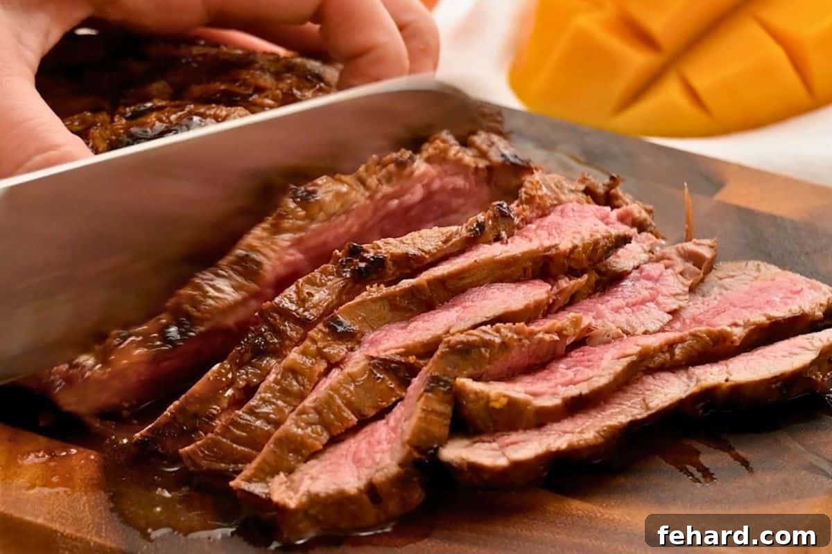 Knife cutting perpendicular to the fibers of the meat across marinated and grilled flank steak.