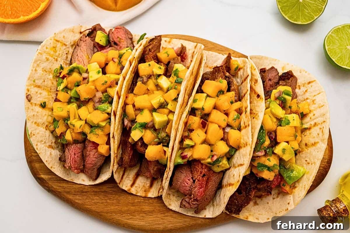 4 soft tortillas filled with sliced grilled marinated flank steak and topped with mango avocado salsa next to fresh mango.