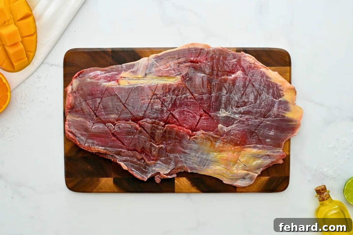 Flank steak on wooden cutting board lightly scored in diamond pattern.