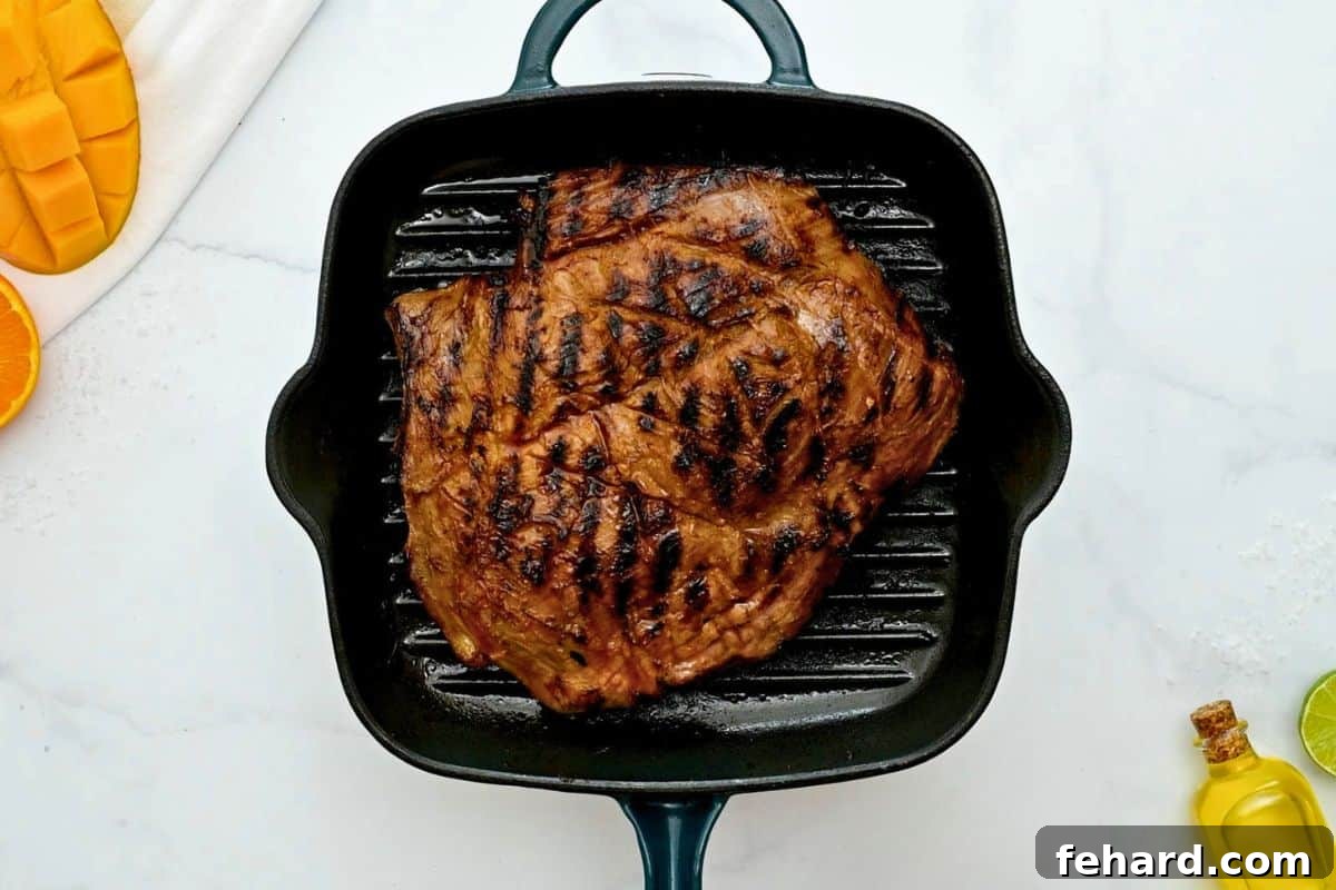 Grilled marinated flank steak on grill pan with scoring marks.