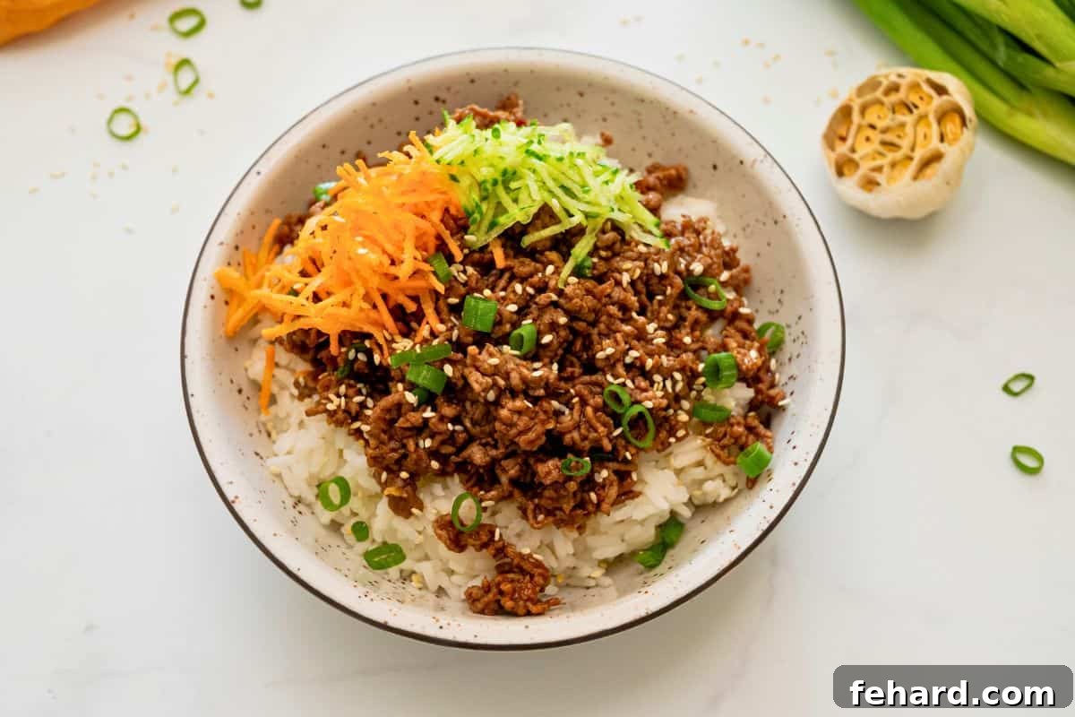 Korean-Style Ground Beef Recipe 3 Ground beef with gochujang sauce served over fluffy white rice and topped with grated carrots and cucumbers and sliced green onions.