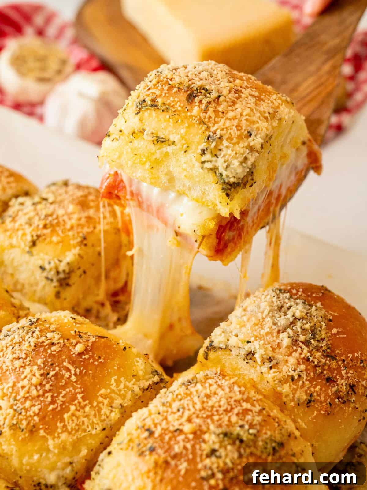 Baked slider made with pizza toppings and garlic butter being picked up showing a melted cheese pull.