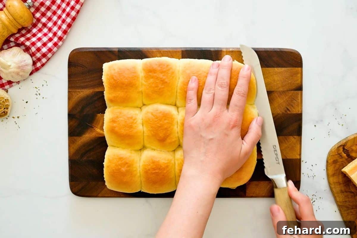 Serrated knife cutting Hawaiian rolls into half horizontally into bottom and top rolls.