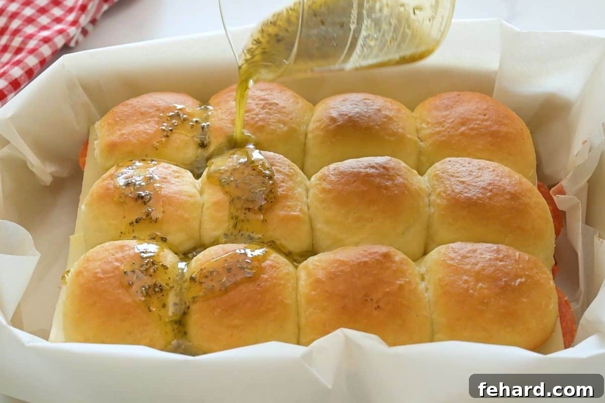 Garlic butter with Italian seasoning being slowly drizzled over assembled pizza sliders.