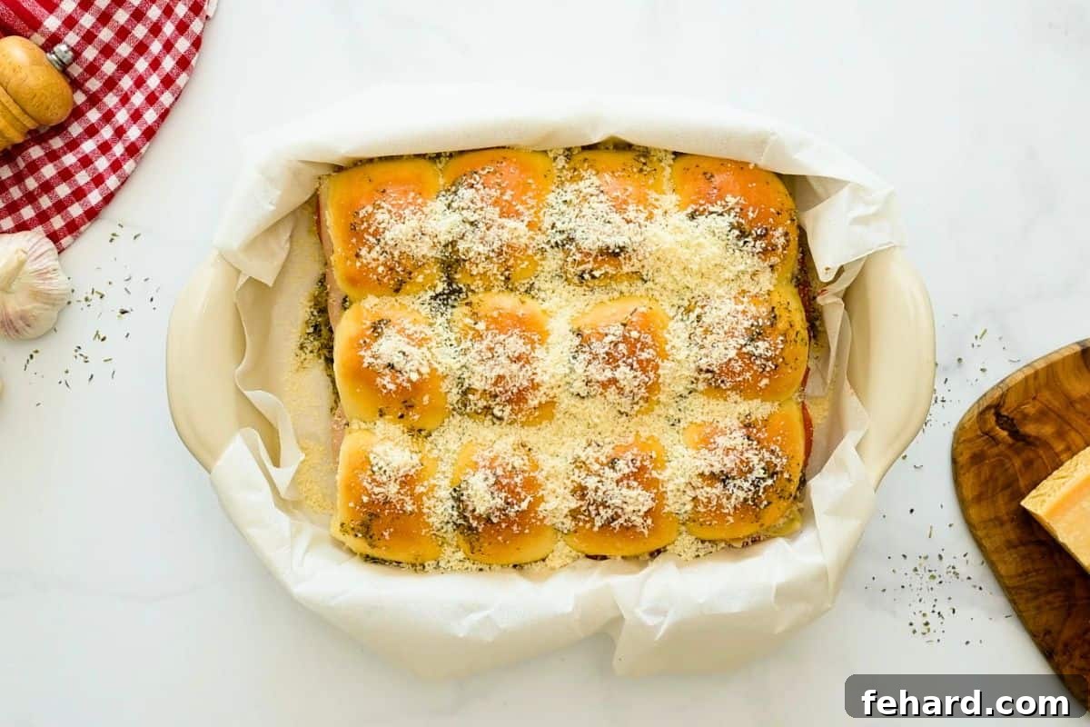 Partially baked pizza sliders in baking dish topped with grated parmesan cheese.