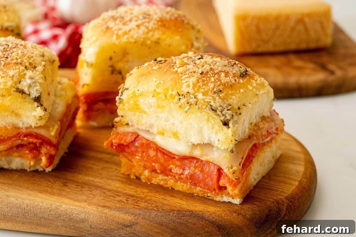 Sliced pizza sliders on wooden cutting board showing layers of provolone, pepperoni, pizza sauce, and mozzarella cheese on garlic butter slider bun.